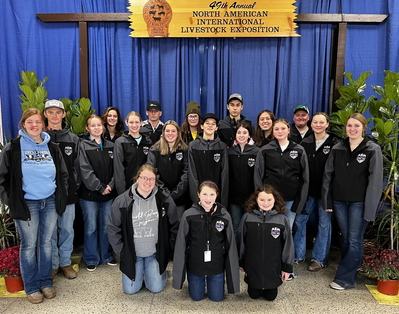 Large group of Belted Galloway Junior Association Members innavy polo shirts and jeans standing in front of blue banner at 2019 North American International Livestock Exposition