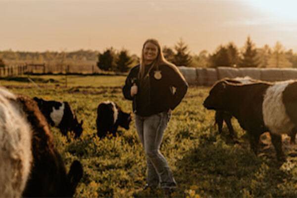 Young woman in dark jacket standing in a field surrounded by cattle